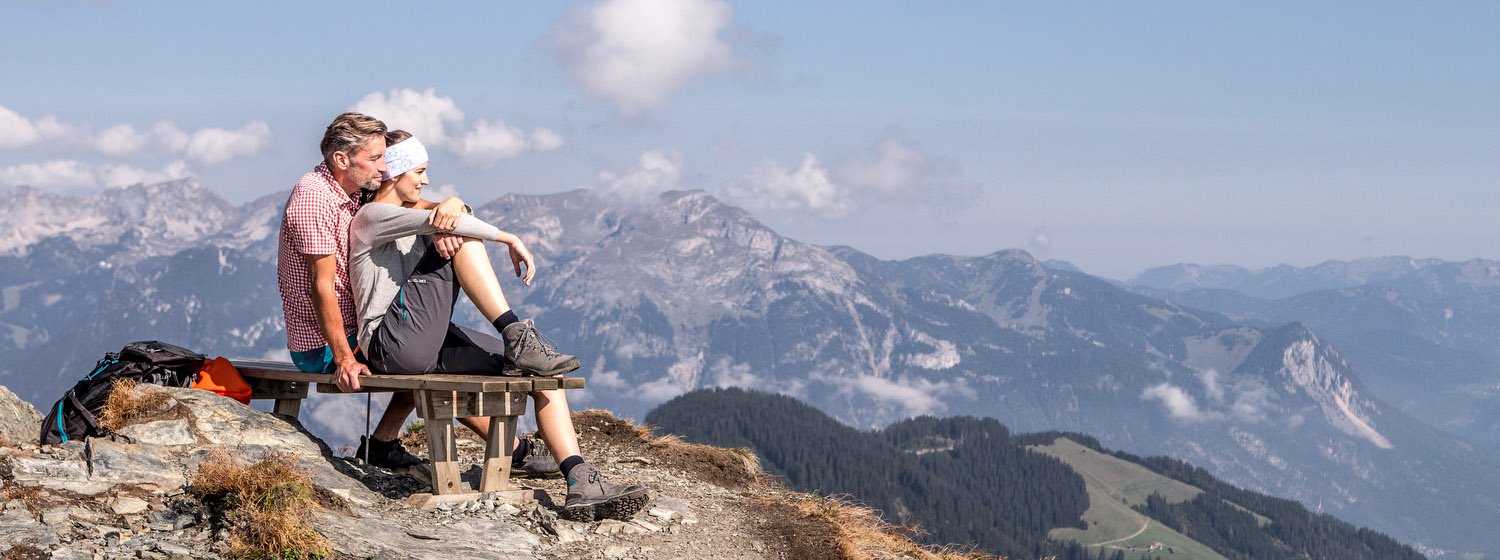 Wanderer machen Pause auf Sitzbank mit Bergpanorama